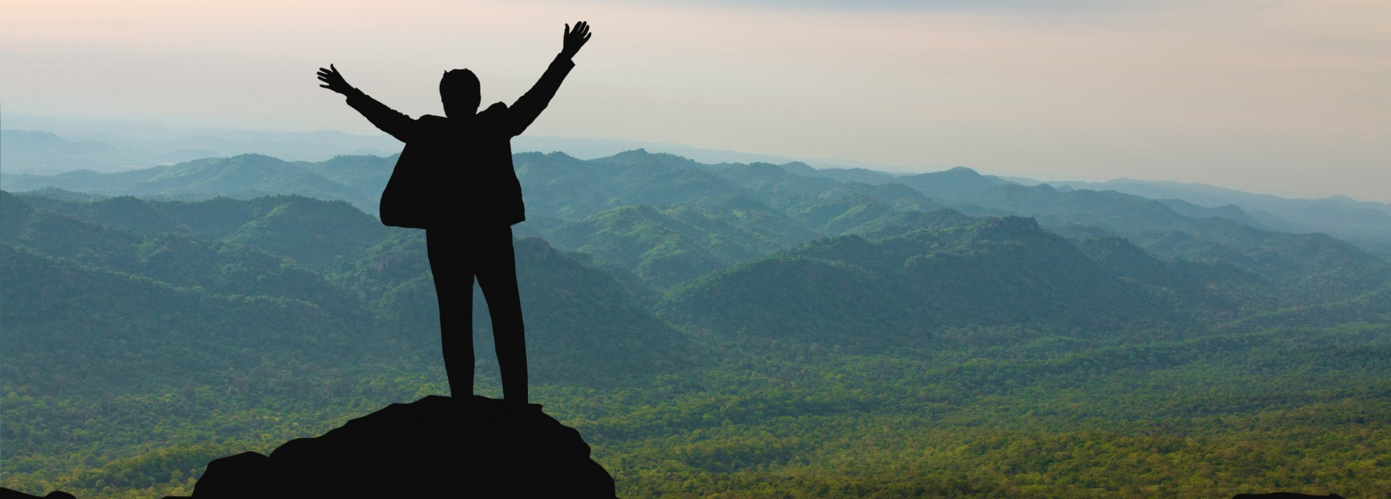 Person celebrating on mountain top with scenic view.